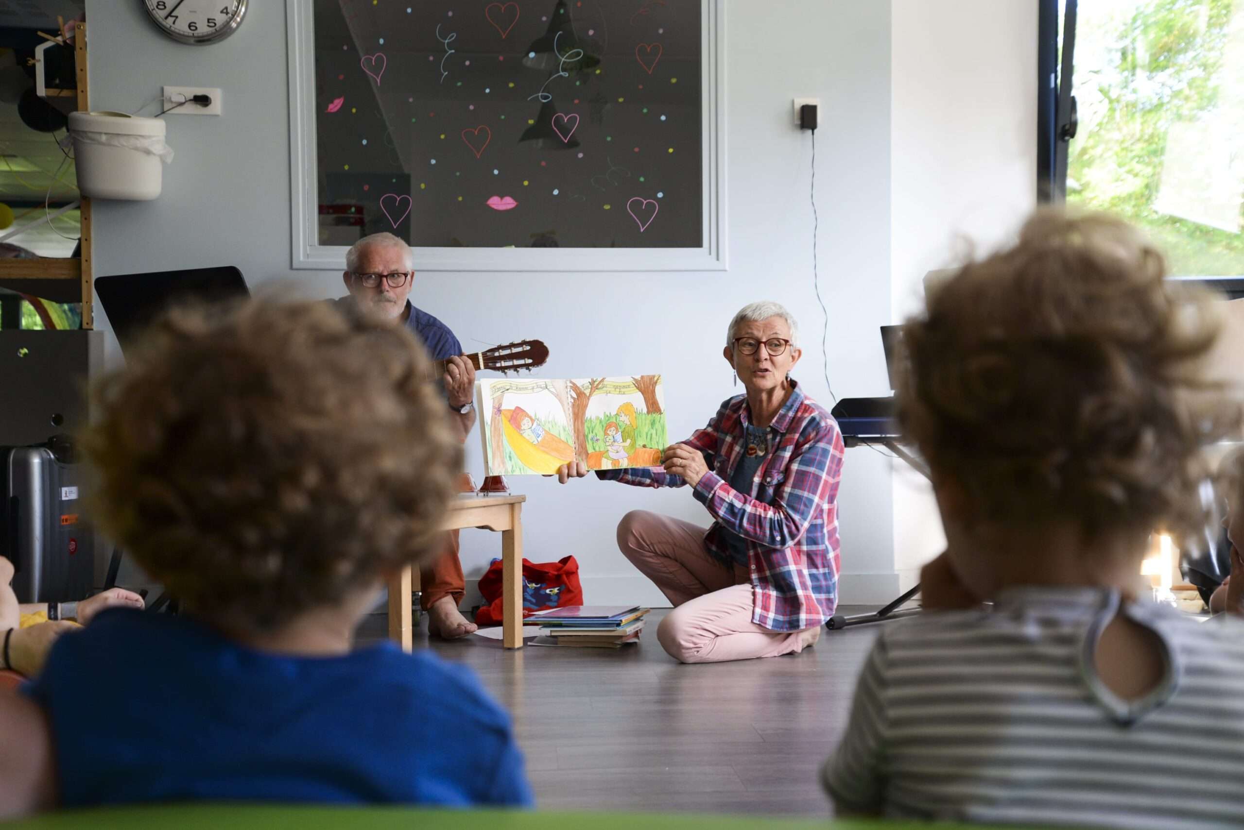 Texte alternatif Deux adultes, un homme et une femme, sont assis devant un groupe d'enfants. L'homme a une guitare et la femme tient un livre de contes illustré qu'elle montre au public.