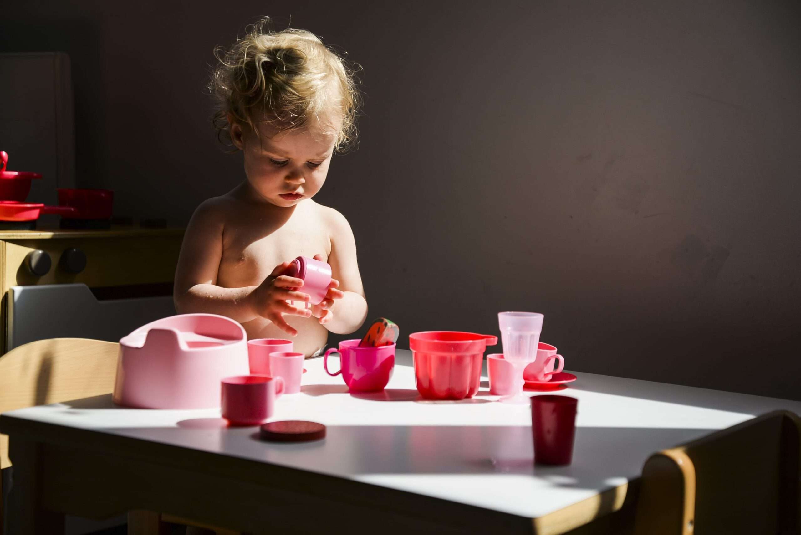 Jeux d’imitation à la crèche Un enfant joue avec une dinette en plastique rose et rouge sur une table, reproduisant les gestes du quotidien.