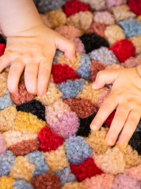 Découverte sensorielle à la crèche Mains d’un enfant posées sur un tapis coloré et moelleux, favorisant l’exploration sensorielle.