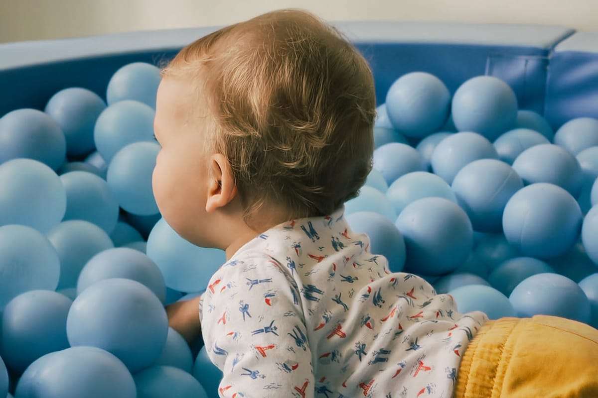 Un jeune enfant joue dans une piscine à balles bleues, allongé et curieux de découvrir son environnement.