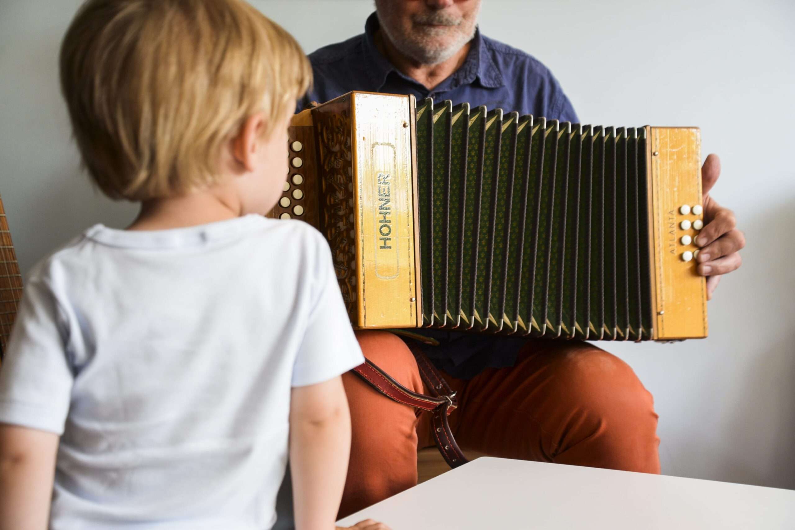 Gros plan sur un enfant blond vu de dos, regardant un homme barbu qui joue de l'accordéon.
