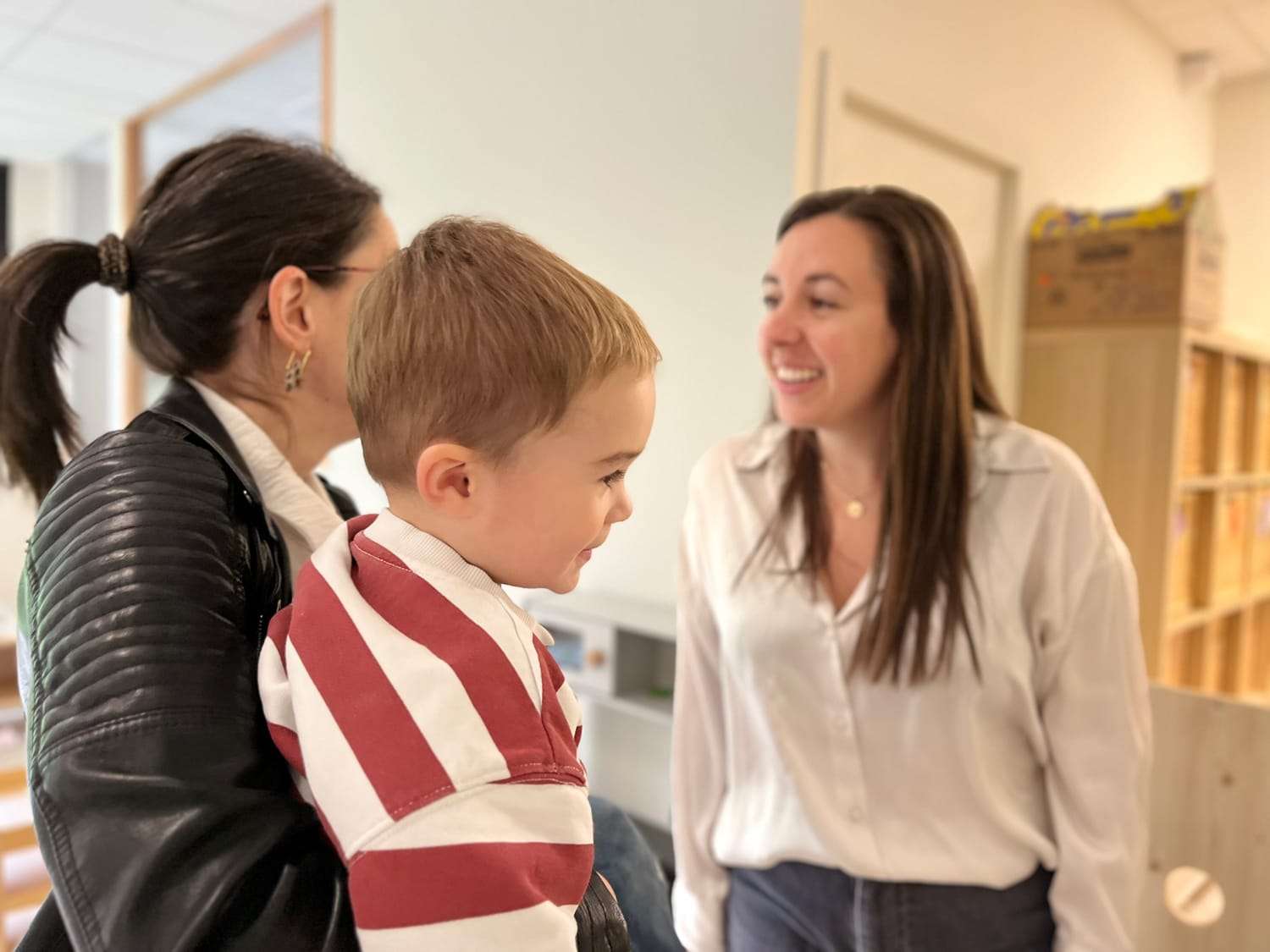 Une éducatrice accueille avec le sourire un enfant et son parent à l’entrée de la crèche.