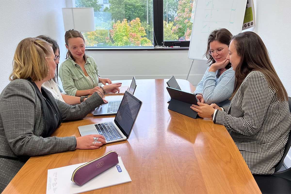 Cinq femmes, membres de l'équipe de la crèche, sont assises autour d'une grande table en bois lors d'une réunion.