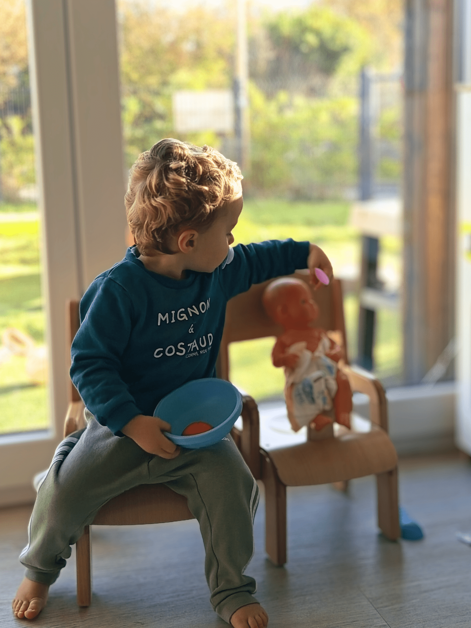 Un jeune garçon assis joue avec un poupée, jeu libre en crèche